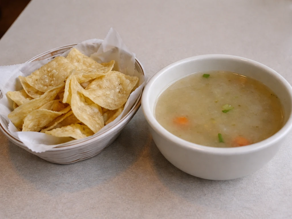 Close-up of a plate of limp chips and a bowl of pale, watery soup on a simple restaurant table.