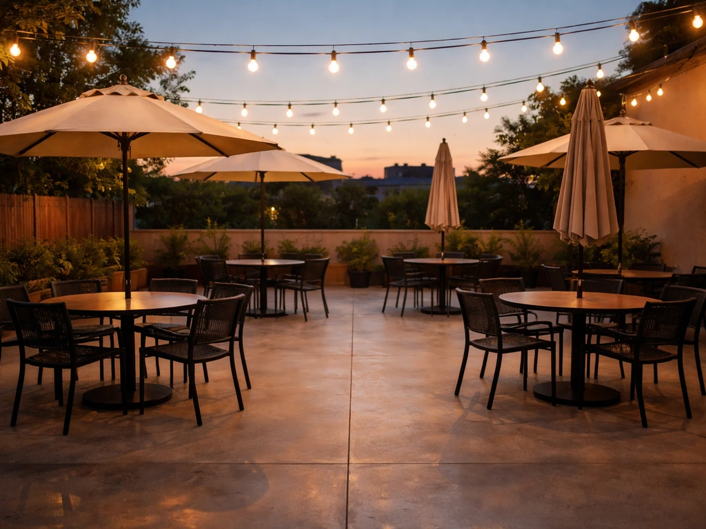Quiet outdoor restaurant patio with umbrellas and warm string lights over empty tables and chairs.